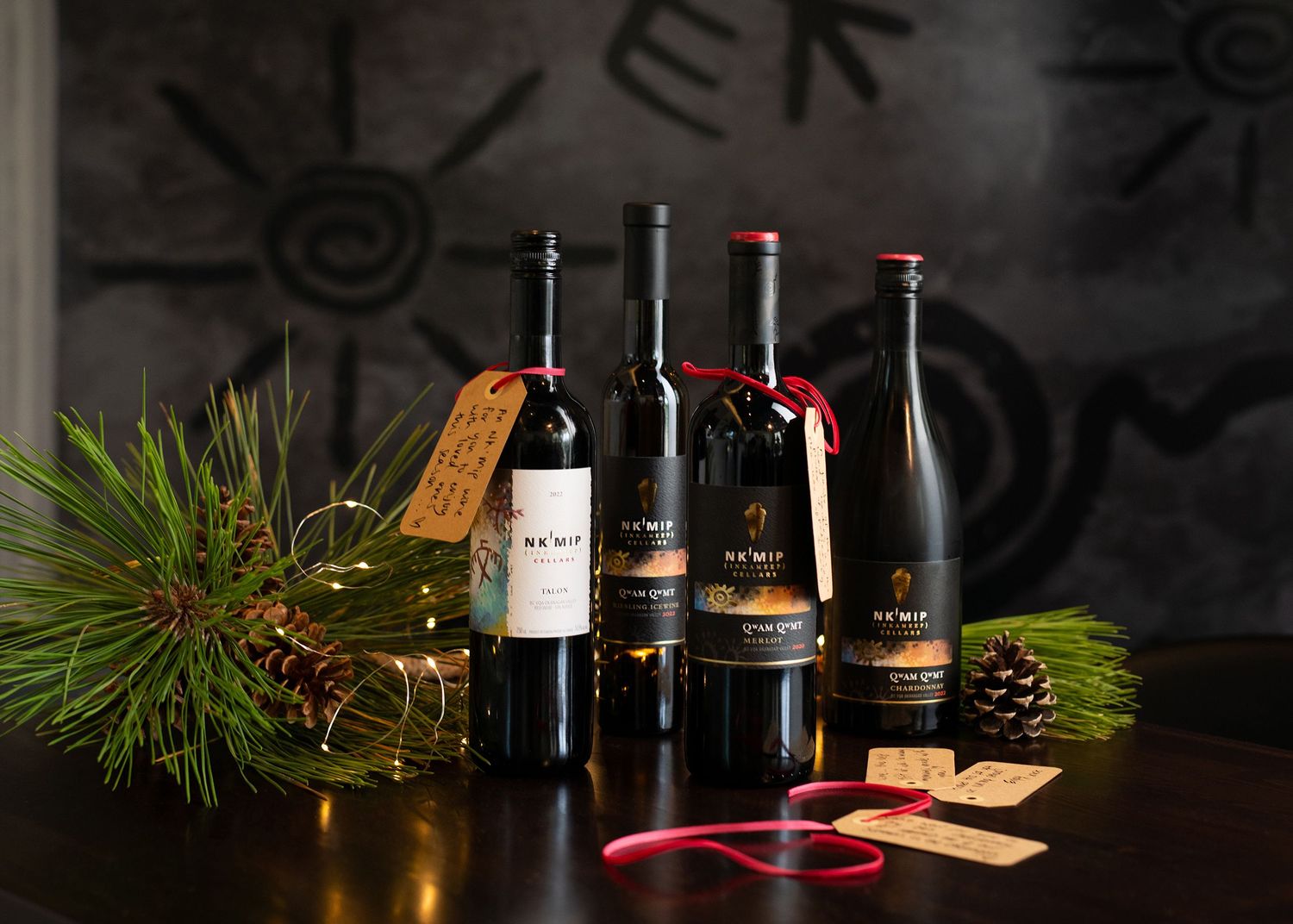 Wine bottles styled with evergreen sprigs, pinecones, and festive ribbon for a seasonal display.