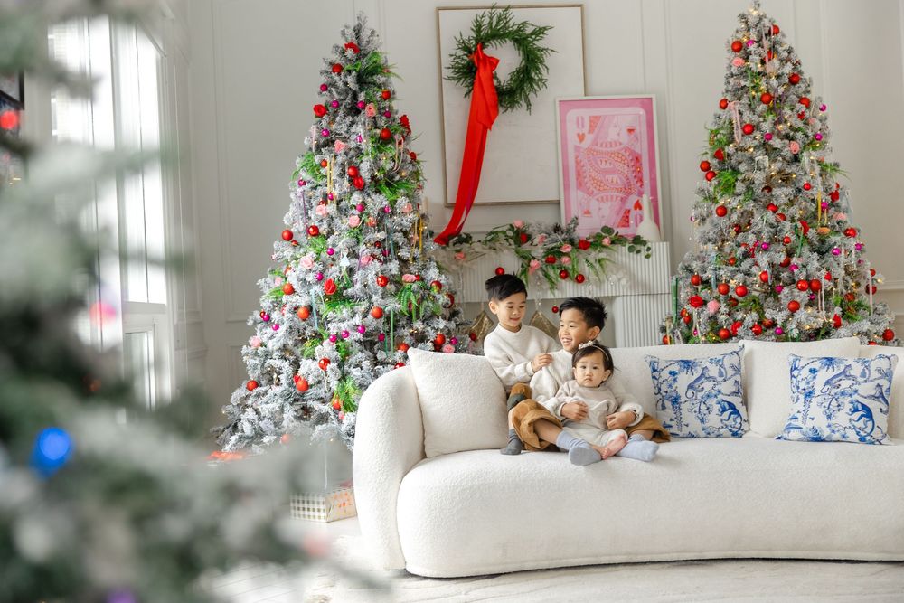 Beautiful white living room holiday scene with two decorated Christmas trees, white couch, and festive holiday decor.