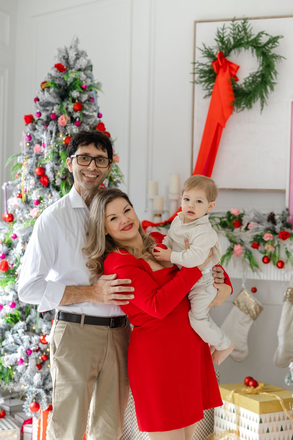 A festive family scene with a decorated Christmas tree, green wreath, and presents in a bright white room.