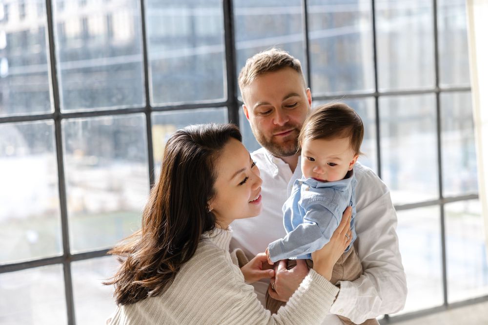 Happy family sharing a joyful moment together by large windows in a bright indoor setting.