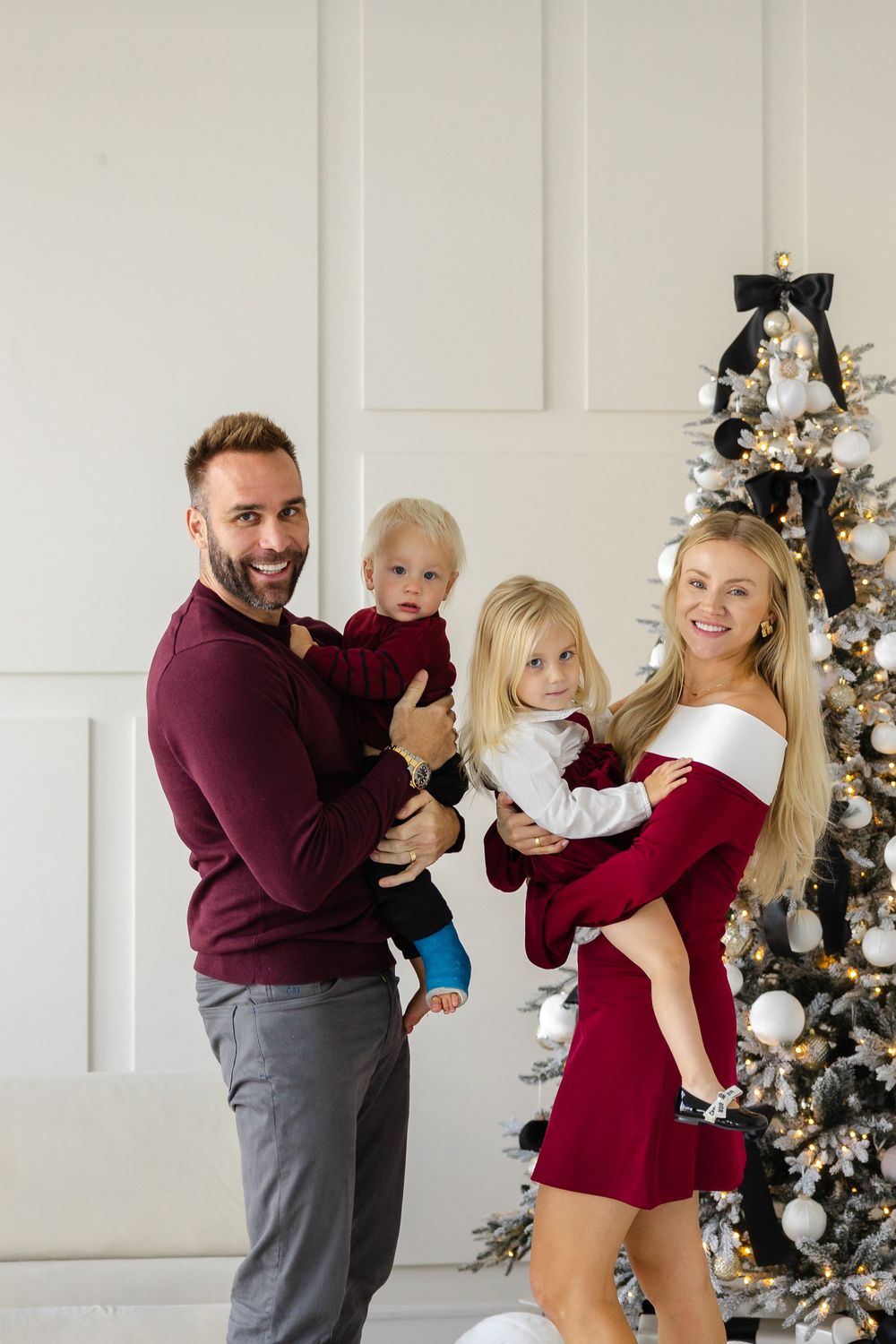 A family shares playful and candid moments in front of a Christmas tree in a modern white room.