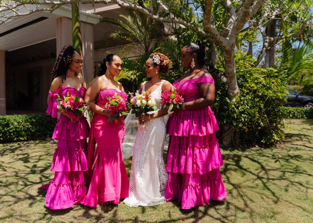 Wedding party in bright fuchsia ruffled dresses pose together outdoors in a tropical garden setting.