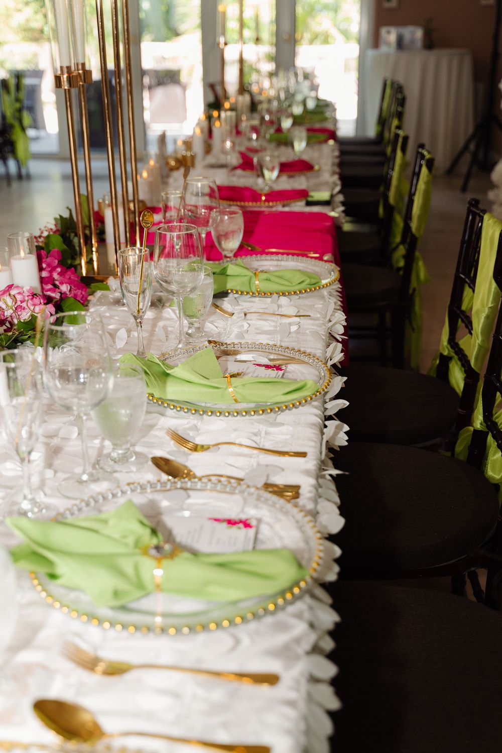 Elegant wedding reception table set with gold flatware, pink napkins and green accents.