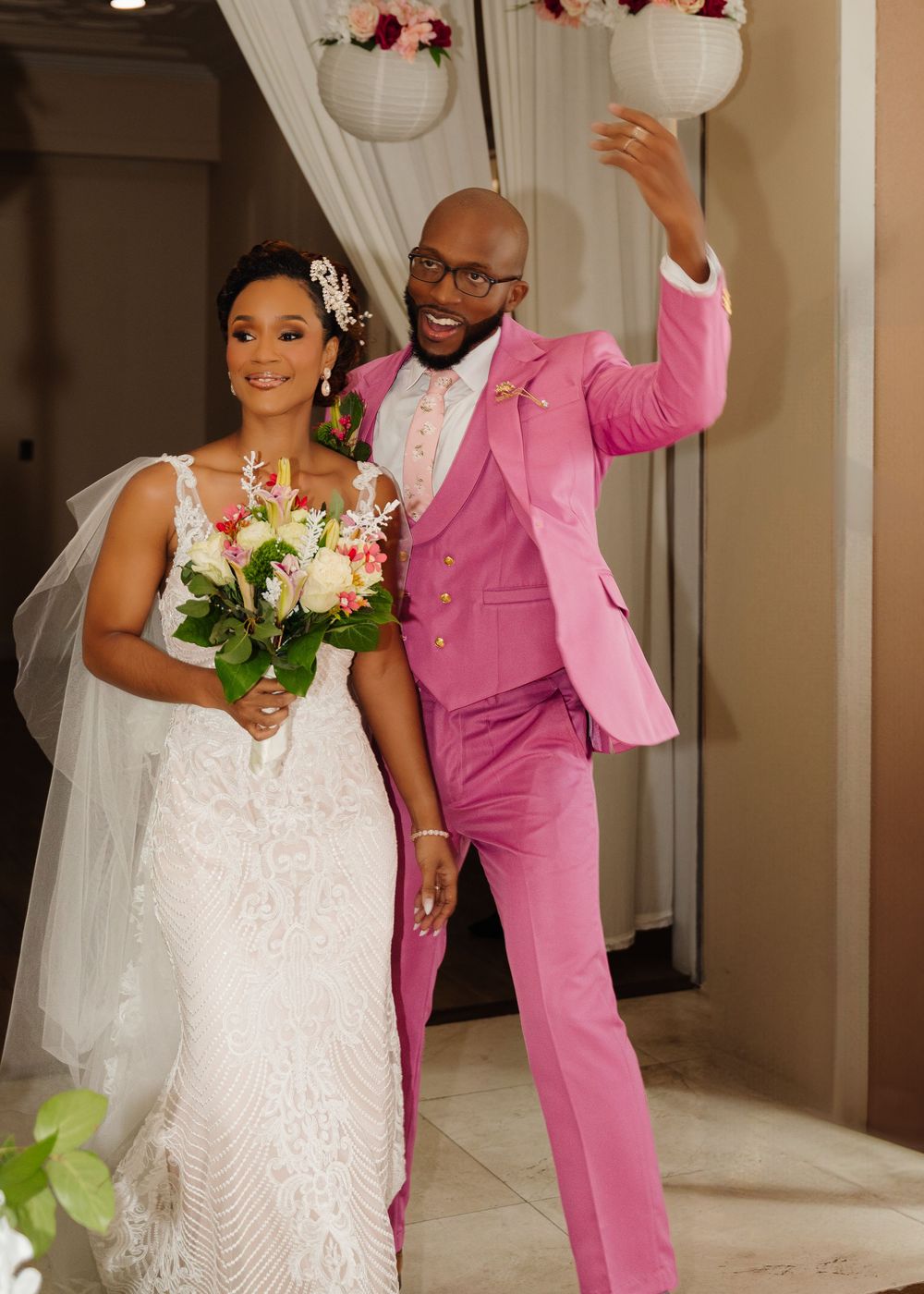 Newlywed couple in white dress and pink suit celebrating joyfully during their wedding reception.