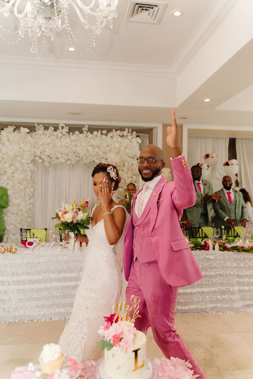 Wedding celebration in an elegant white ballroom with chandelier and floral decorations.