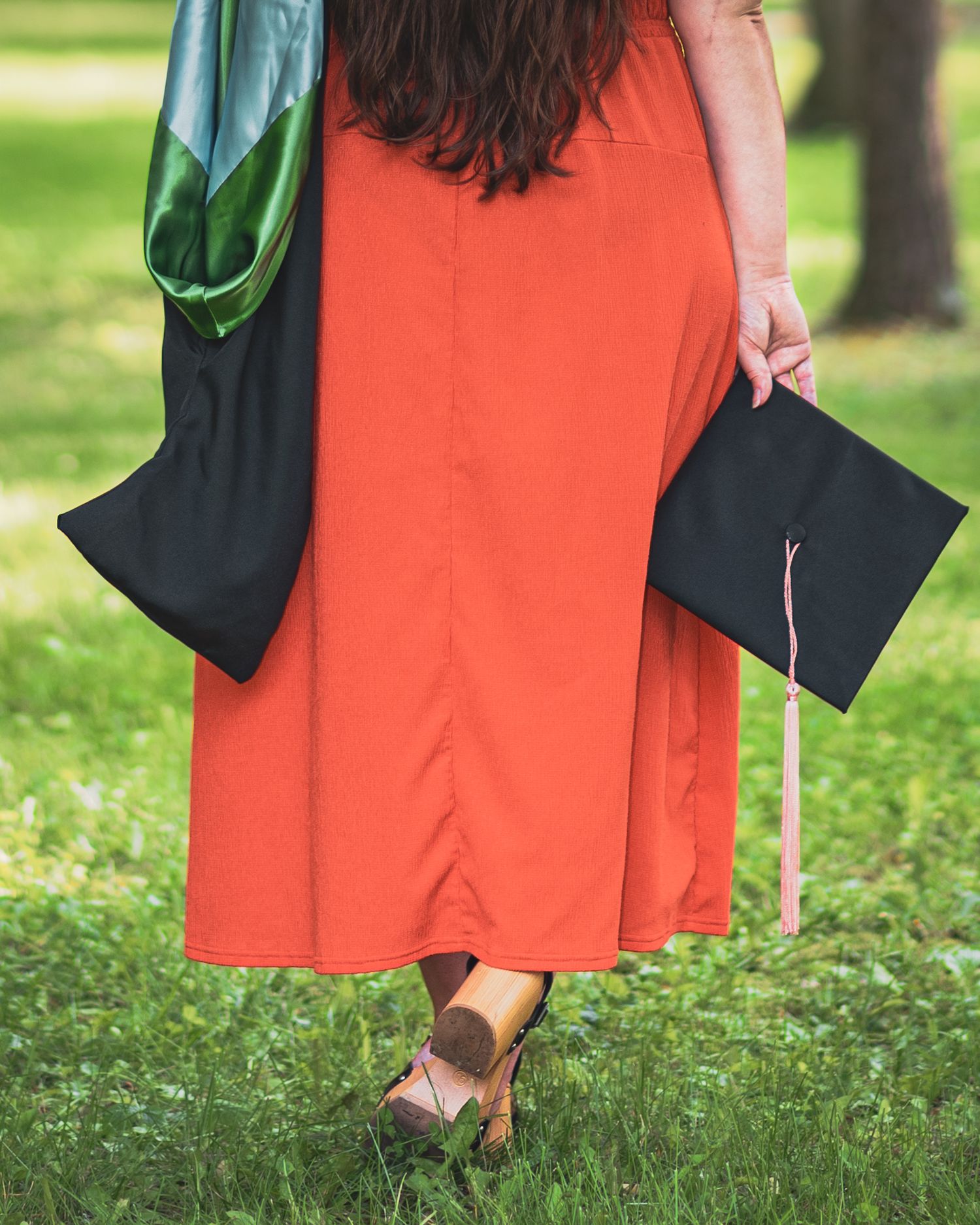 Close-up of graduation gowns and heels on grass during commencement ceremony.