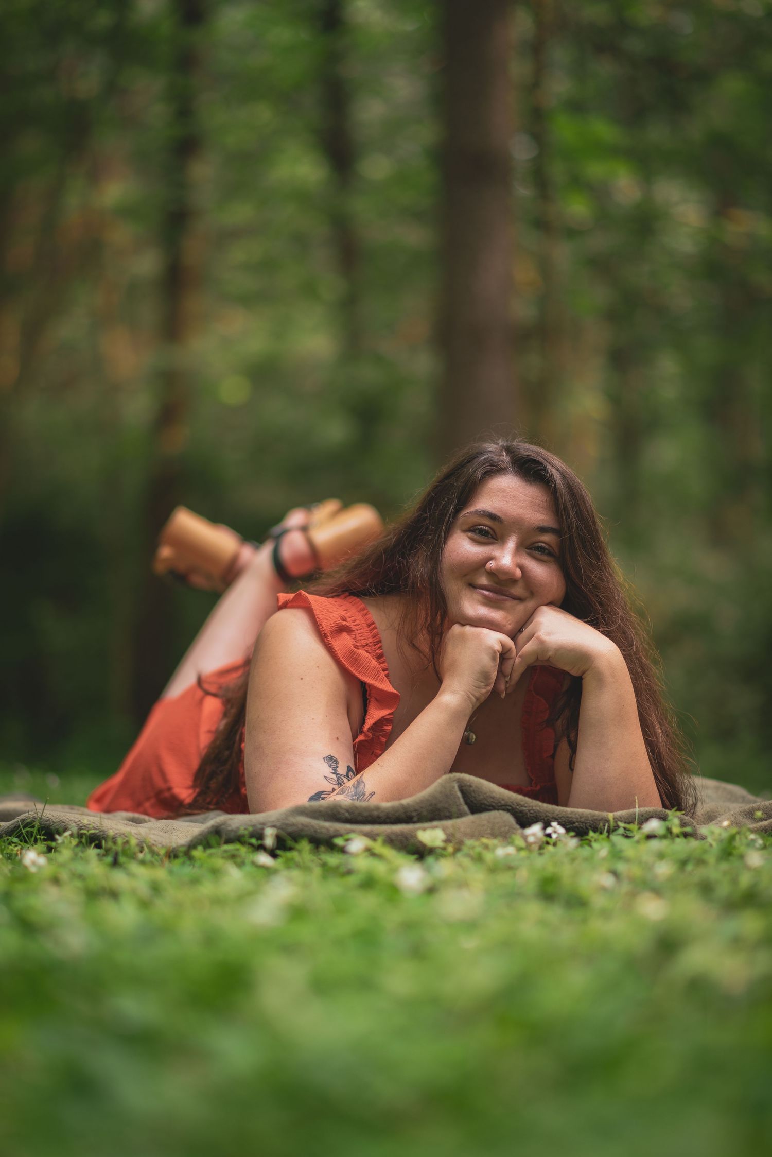 Graduate in red dress relaxes on ground during forest photo session.