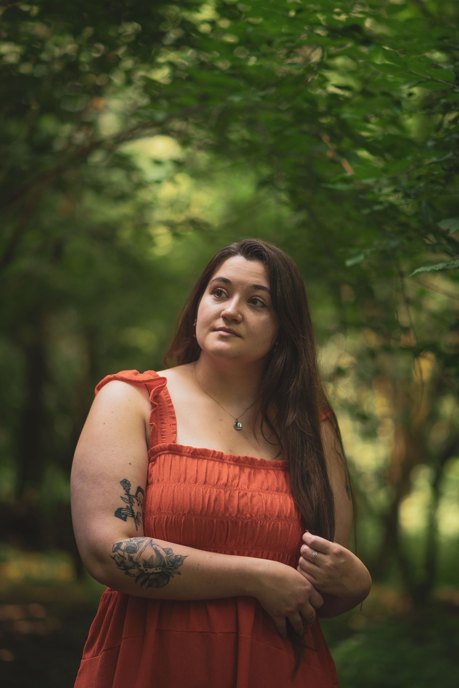 A person wearing a coral sundress stands against a backdrop of green foliage.