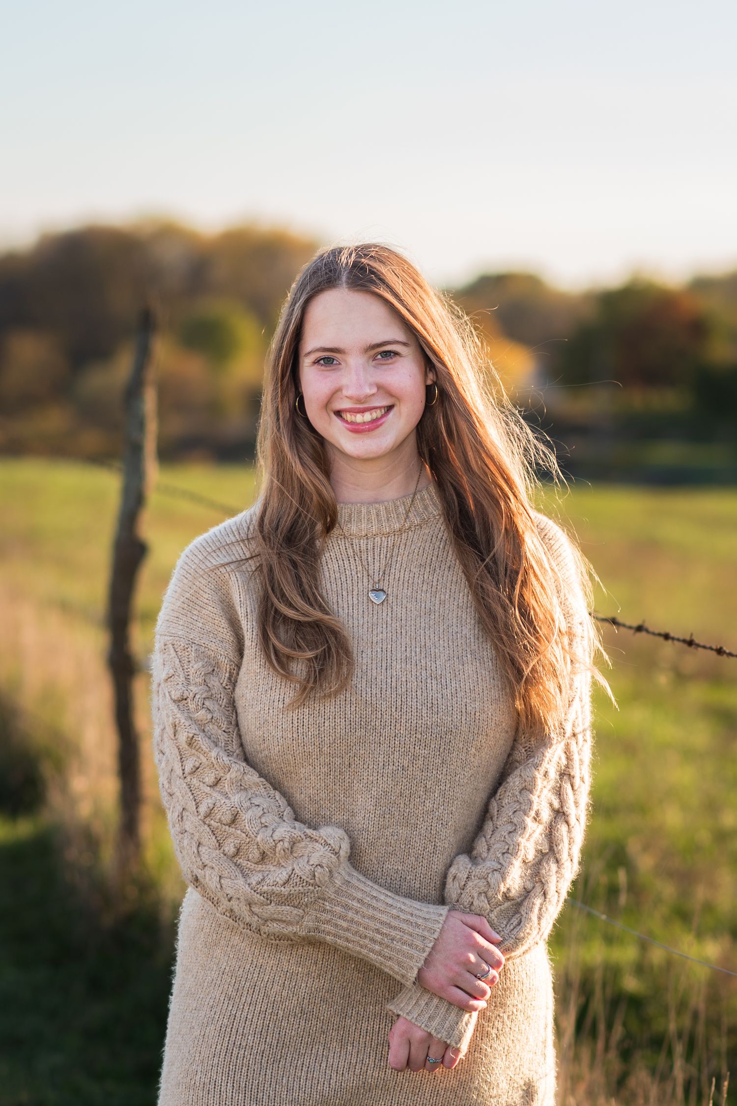 A person in a beige knit sweater poses in a sunlit field at golden hour.