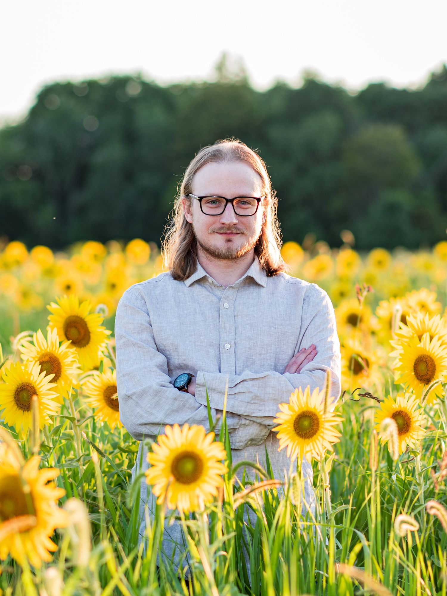 Person in light colored shirt standing among vibrant yellow sunflowers in summer field.