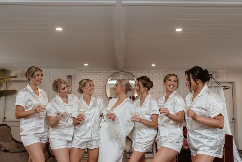A group of people in white chef coats smiling and laughing together in a bright indoor setting.