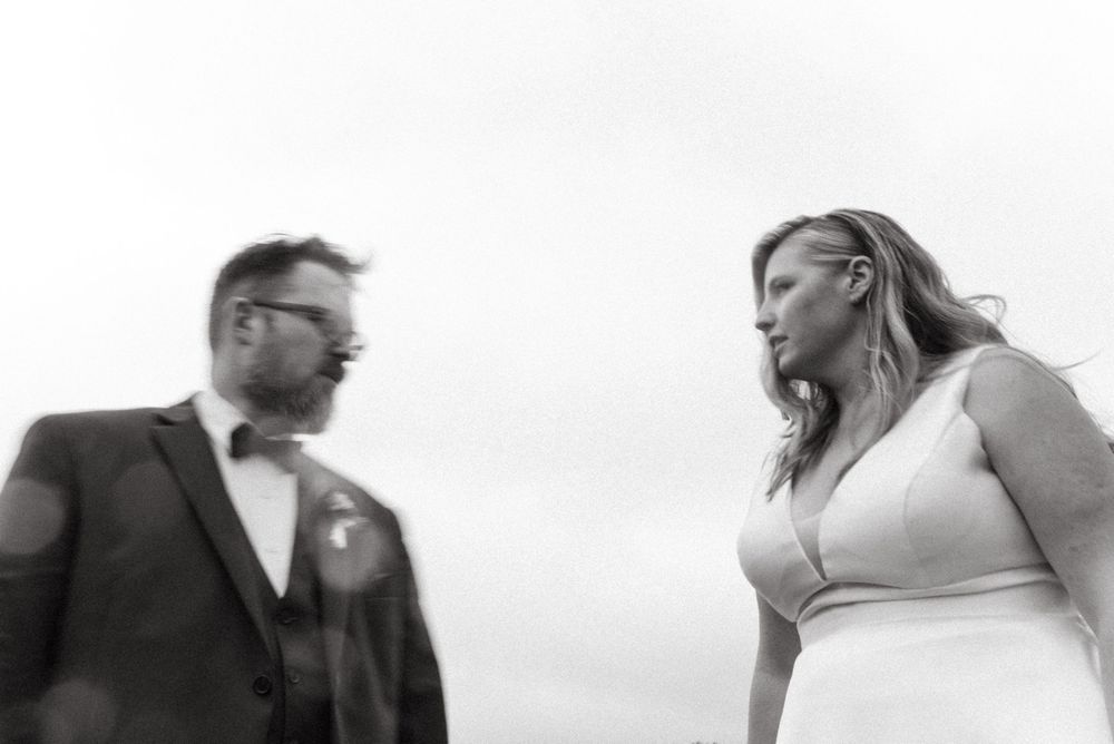 Artistic black and white low angle photo of a couple looking at each other against cloudy sky.
