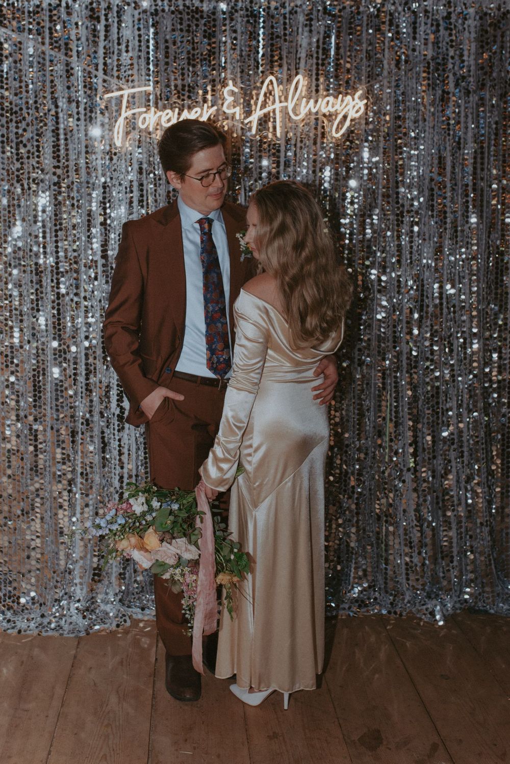 A couple stands against a sparkly silver backdrop at a wedding, shown in a series of romantic poses.