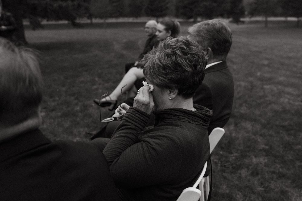 A photographer in dark clothing takes pictures outdoors in a black and white photograph.