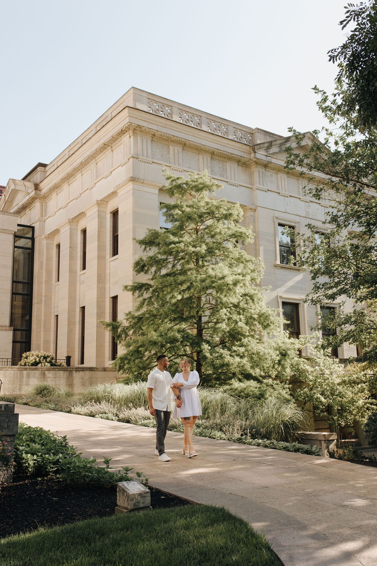 Couple holding hands in front of Ohio Statehouse during golden morning light.