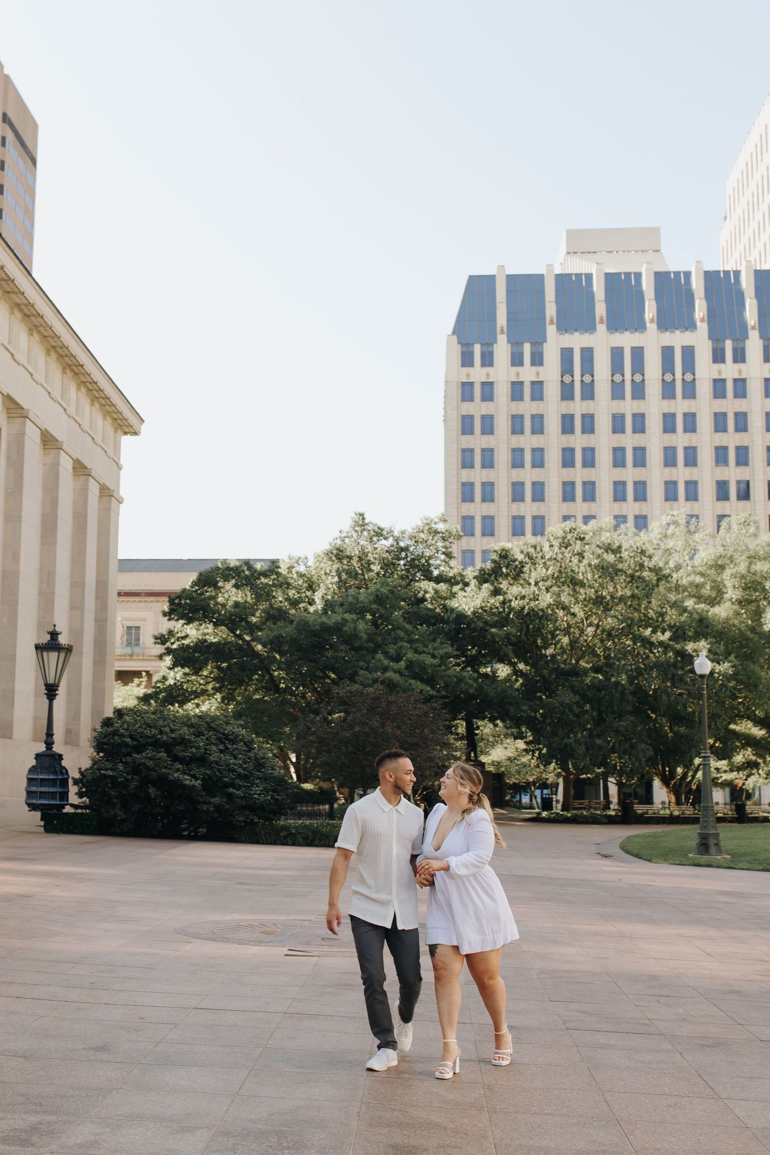 Couple playfully walking into each other in front of tall columns and historic steps in downtown Columbus during their engagement photos.