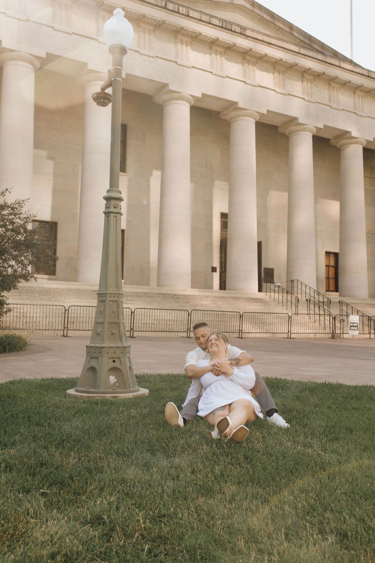 Engaged couple sitting together in front of a black iron lamppost outside the Ohio Statehouse