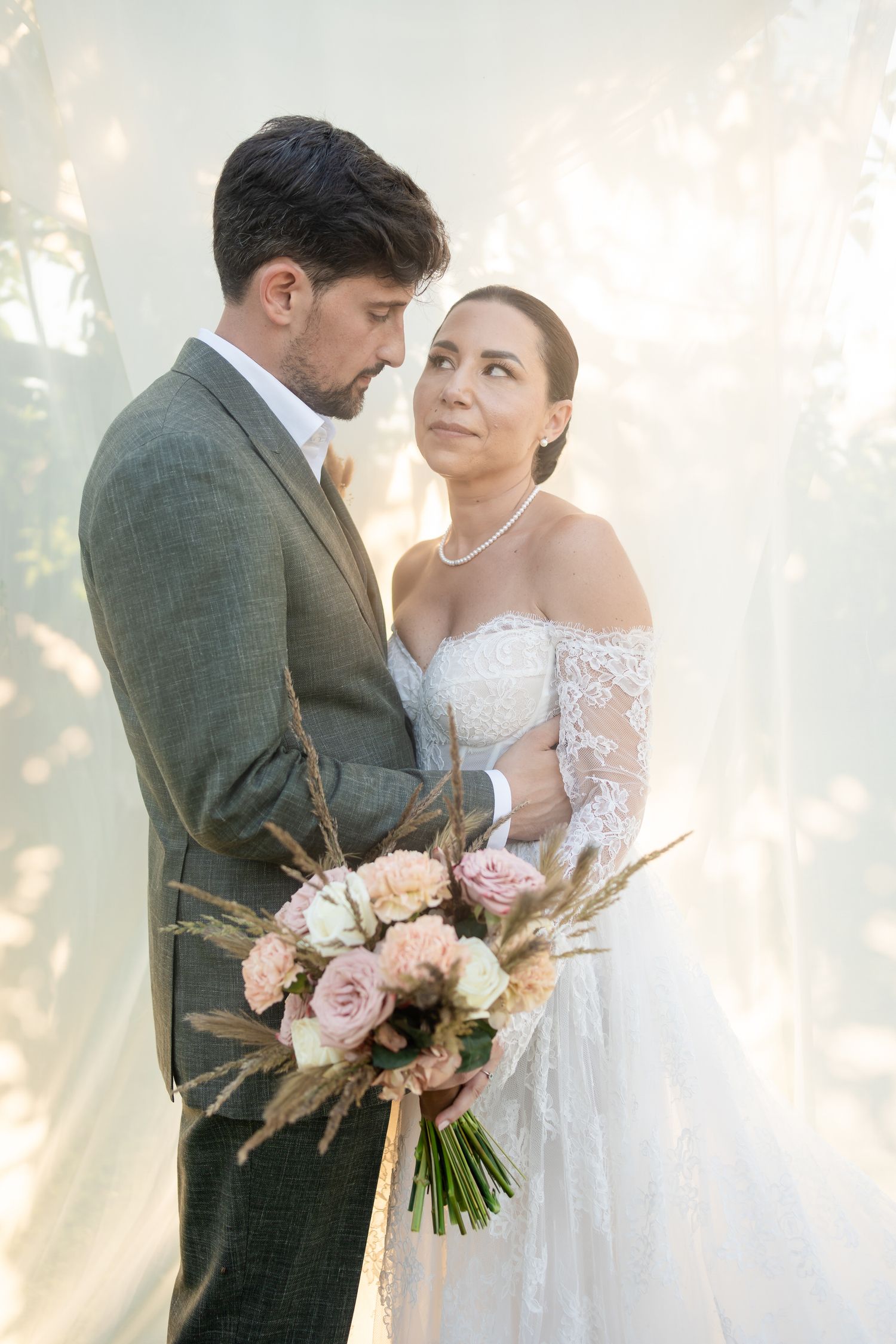 Romantic wedding portrait with soft sunlight filtering through trees and pink floral bouquet.