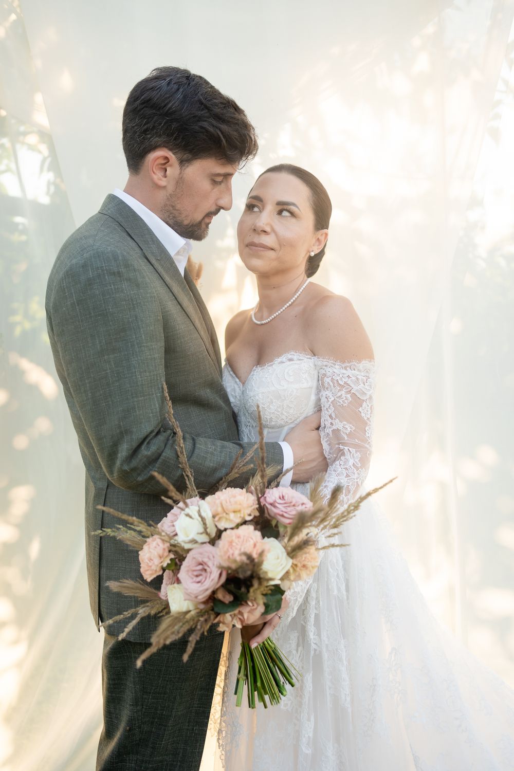 Romantic wedding portrait with soft sunlight filtering through trees and pink floral bouquet.