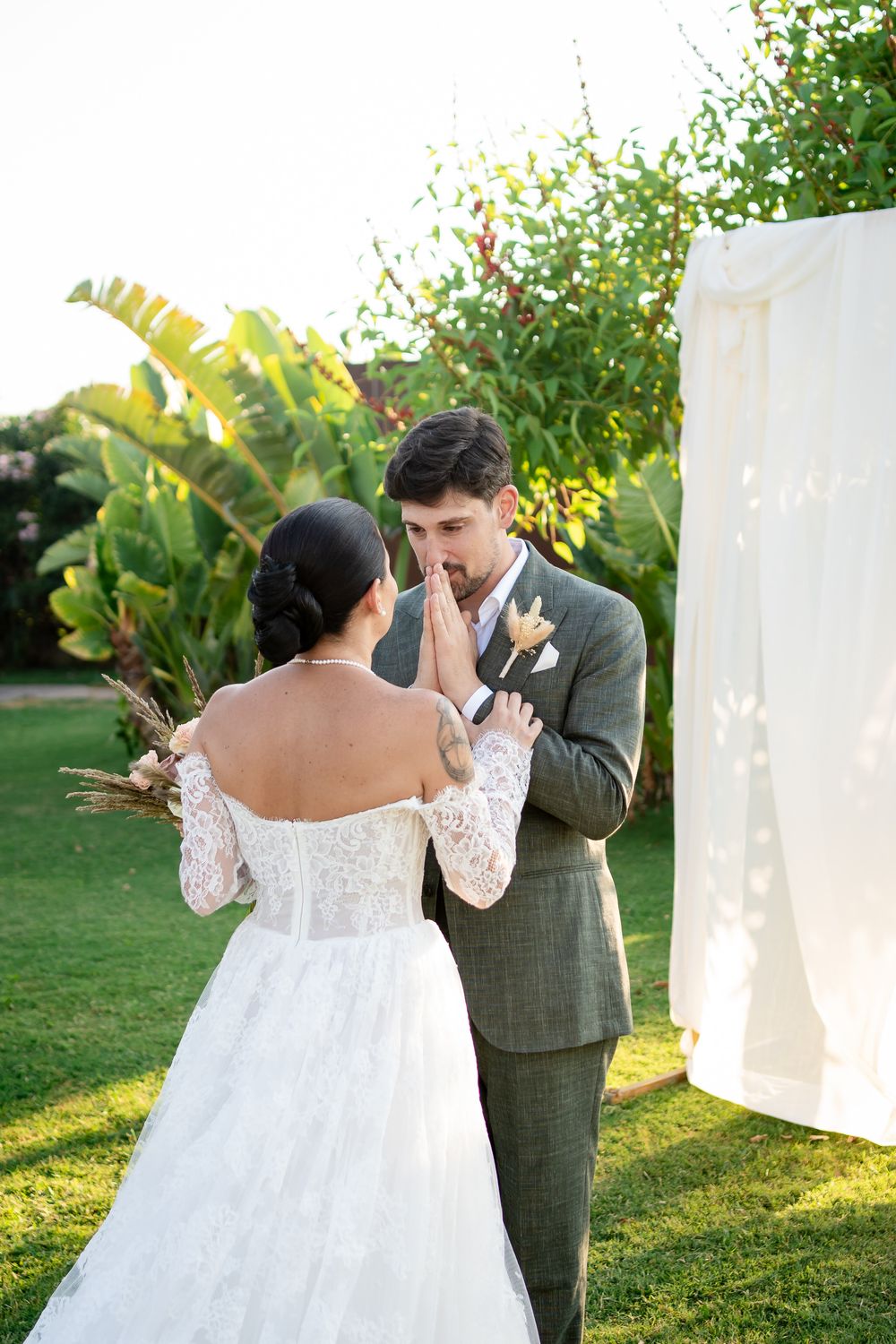 A couple shares their first look reaction in a garden setting with white fabric panels.