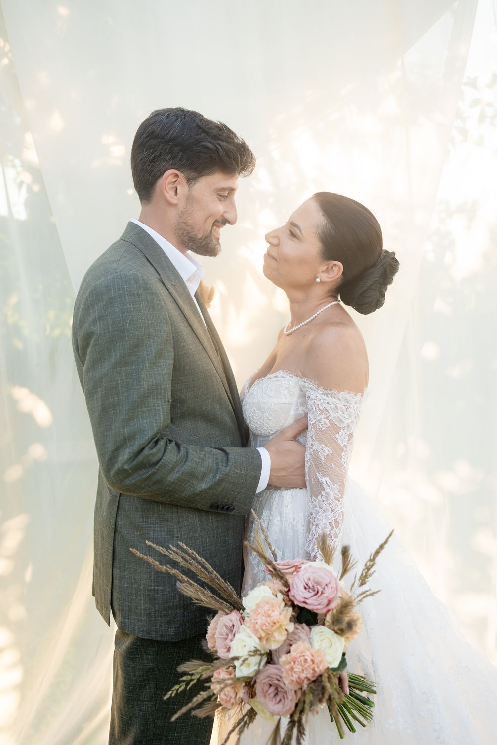 A romantic wedding portrait with soft lighting and white fabric backdrop showing tender moments between the couple.