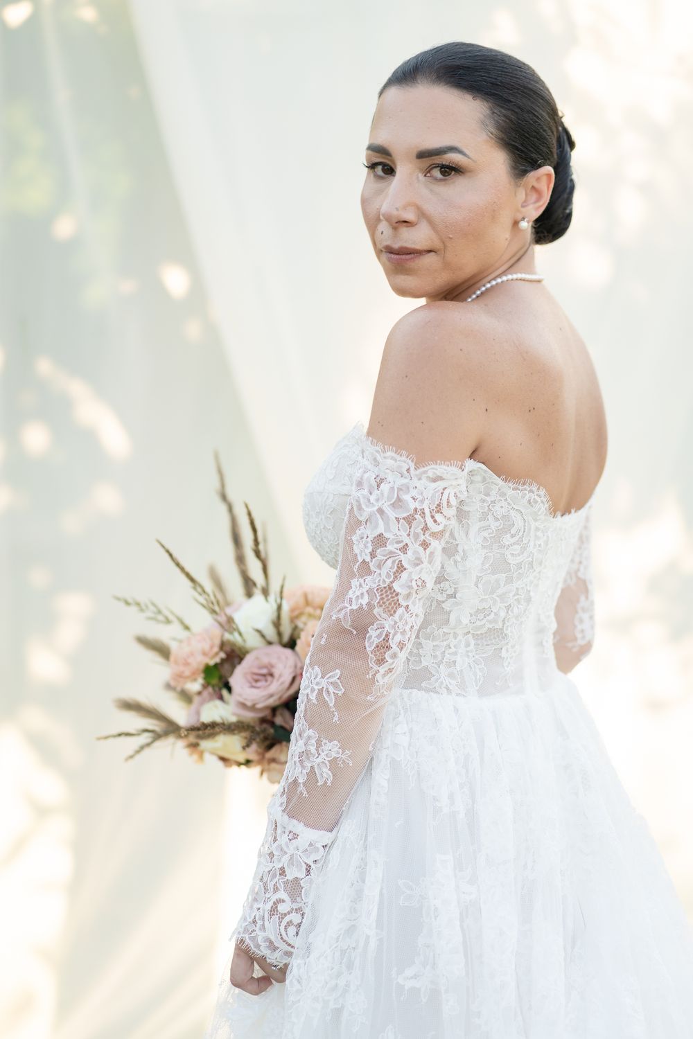 Close-up of bride in detailed lace sleeve wedding dress holding romantic bouquet.