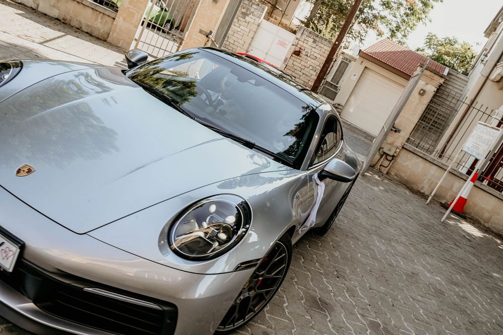 Silver Porsche 911 sports car parked on a street with buildings and palm trees in the background.