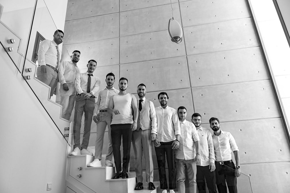 A group of people in formal white and grey attire stand in a diagonal line formation on modern stairs.
