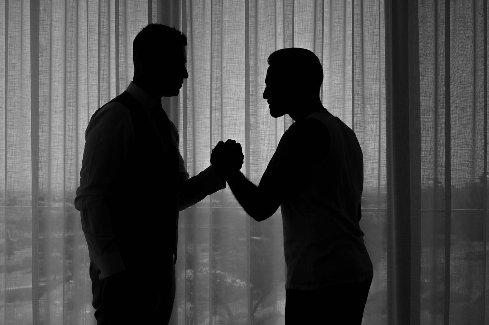 Silhouetted group of people stand in front of vertical blinds in a black and white photo.