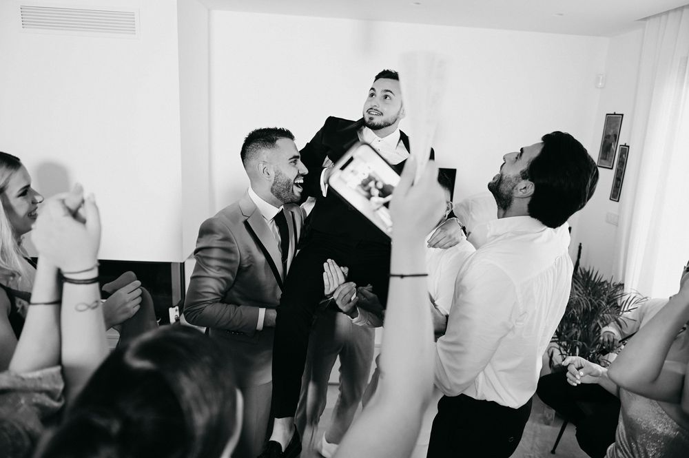 Black and white photo showing a group celebrating at a party with raised glasses in a bright interior room.