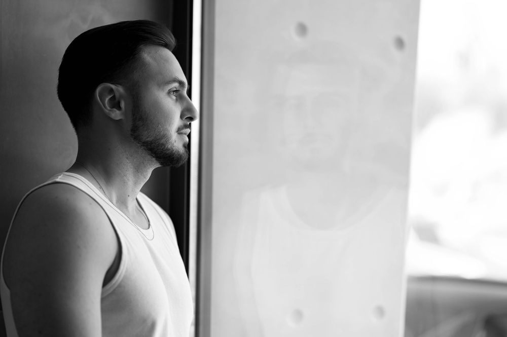 A silhouette gazes thoughtfully through a window while standing in dramatic lighting creating a contemplative scene.