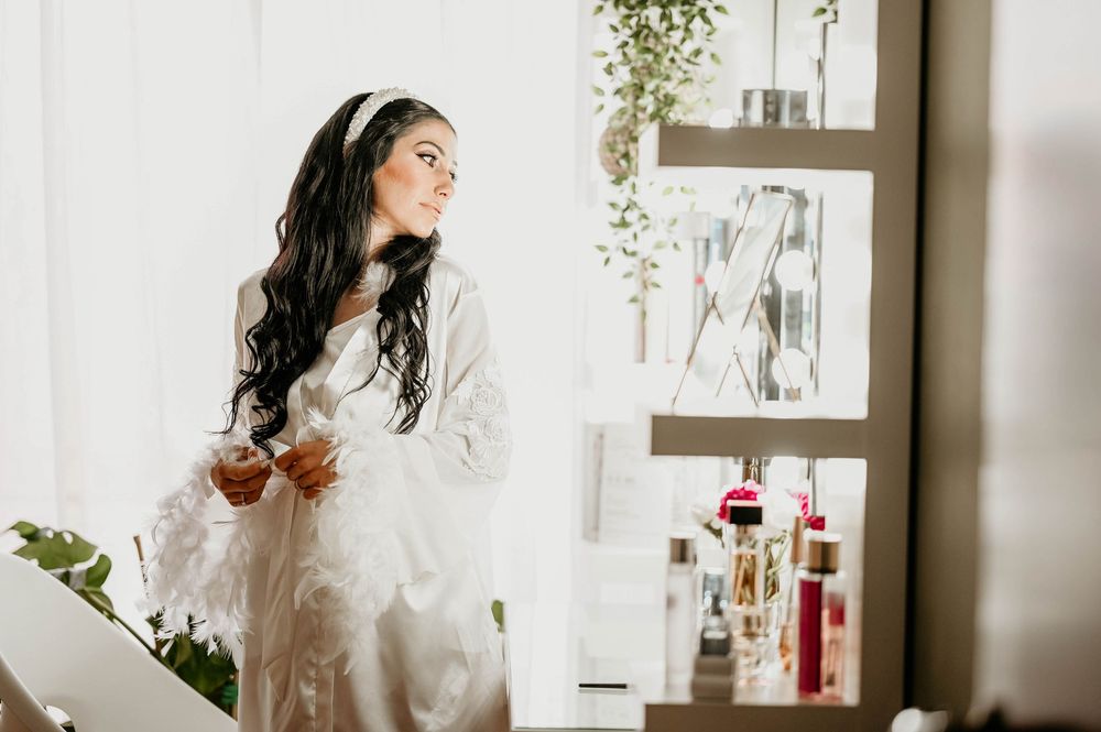 Long dark-haired woman in white sweater poses thoughtfully in bright modern kitchen with greenery and decor.