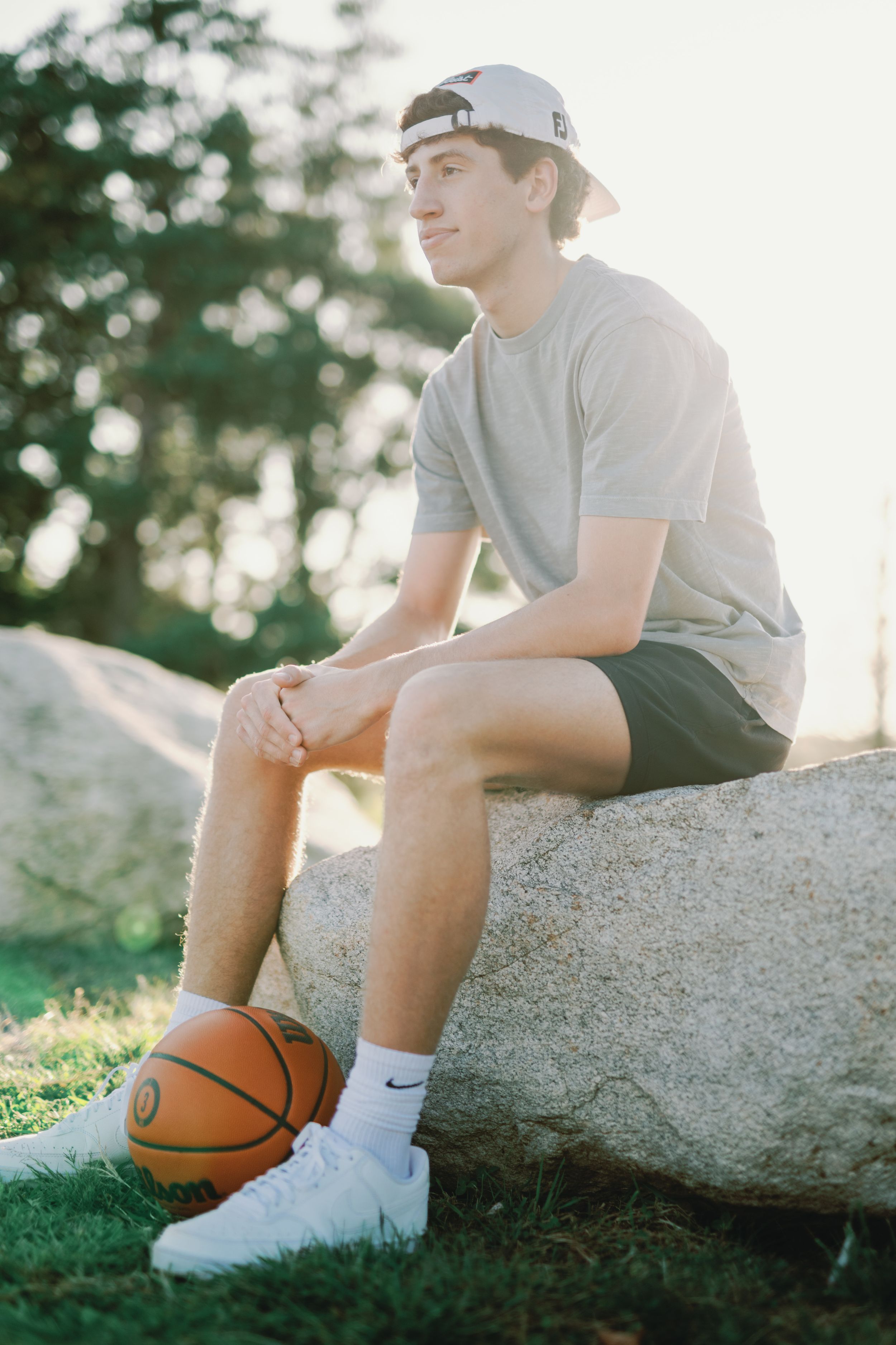 Casual portrait series of a young athlete sitting on a rock with a basketball in outdoor natural lighting.