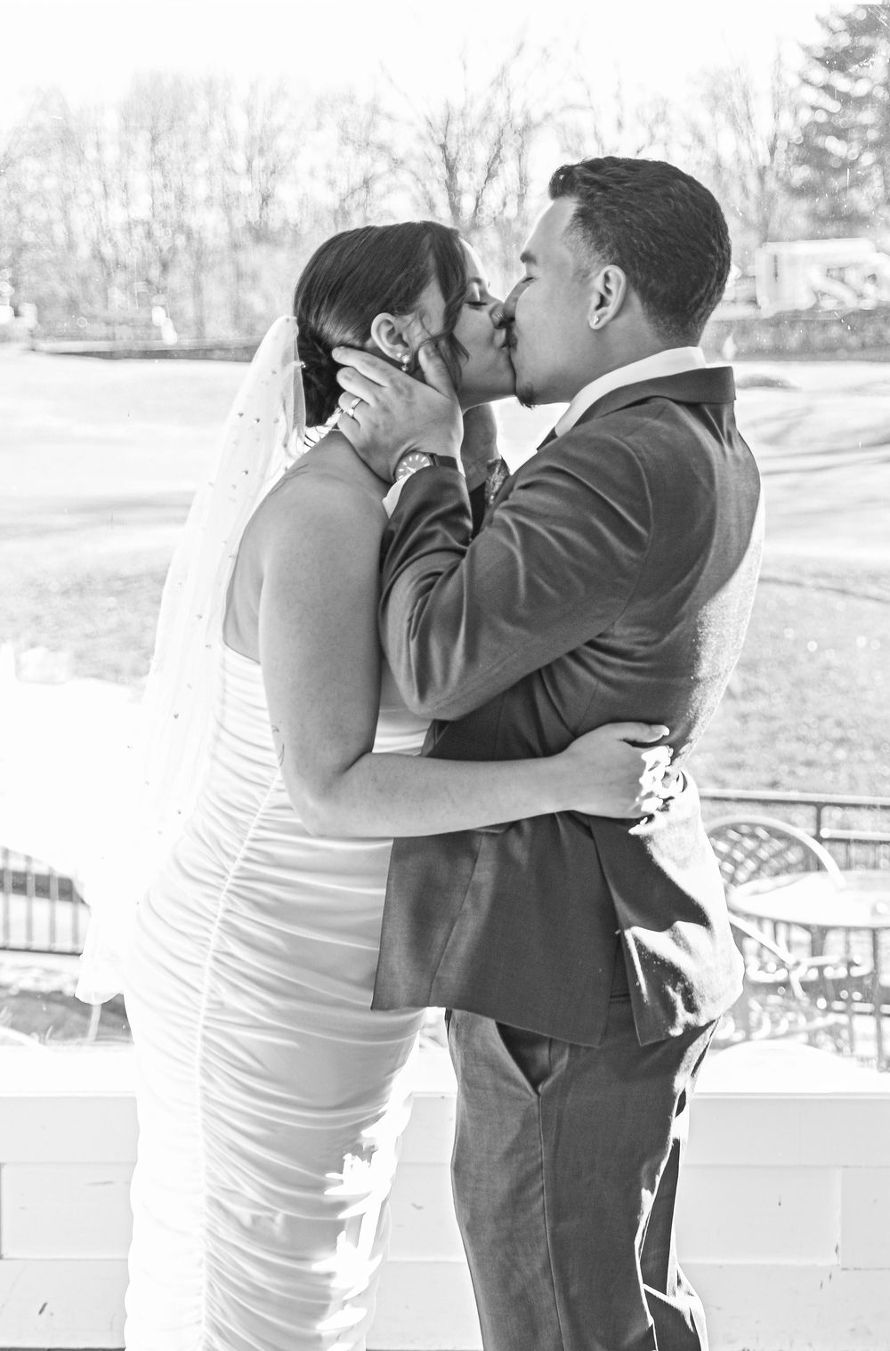 A romantic black and white wedding photograph showing a tender kiss between newlyweds outdoors in winter.