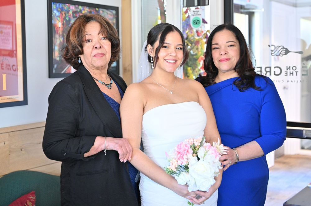 A group of people in formal attire including dresses in white and blue gather together for celebratory photos.