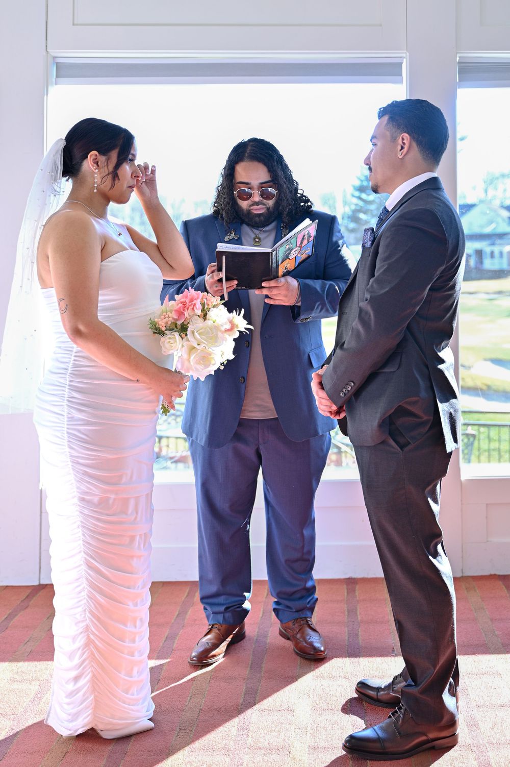 A short person in a suit hugs someone in a white wedding dress during what appears to be a heartfelt moment at a ceremony.