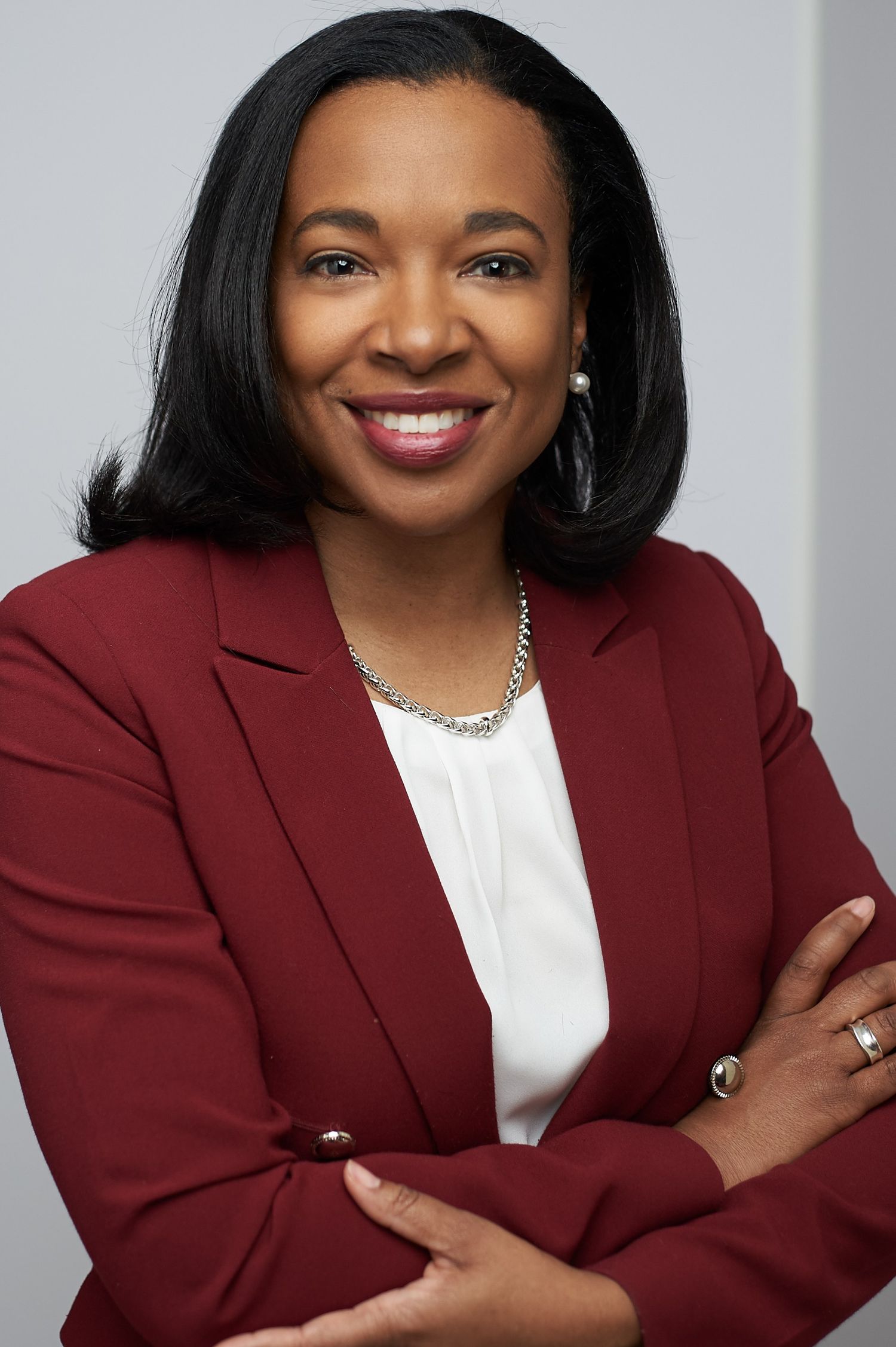 Professional Black woman in a red blazer with arms crossed smiling in a corporate headshot.