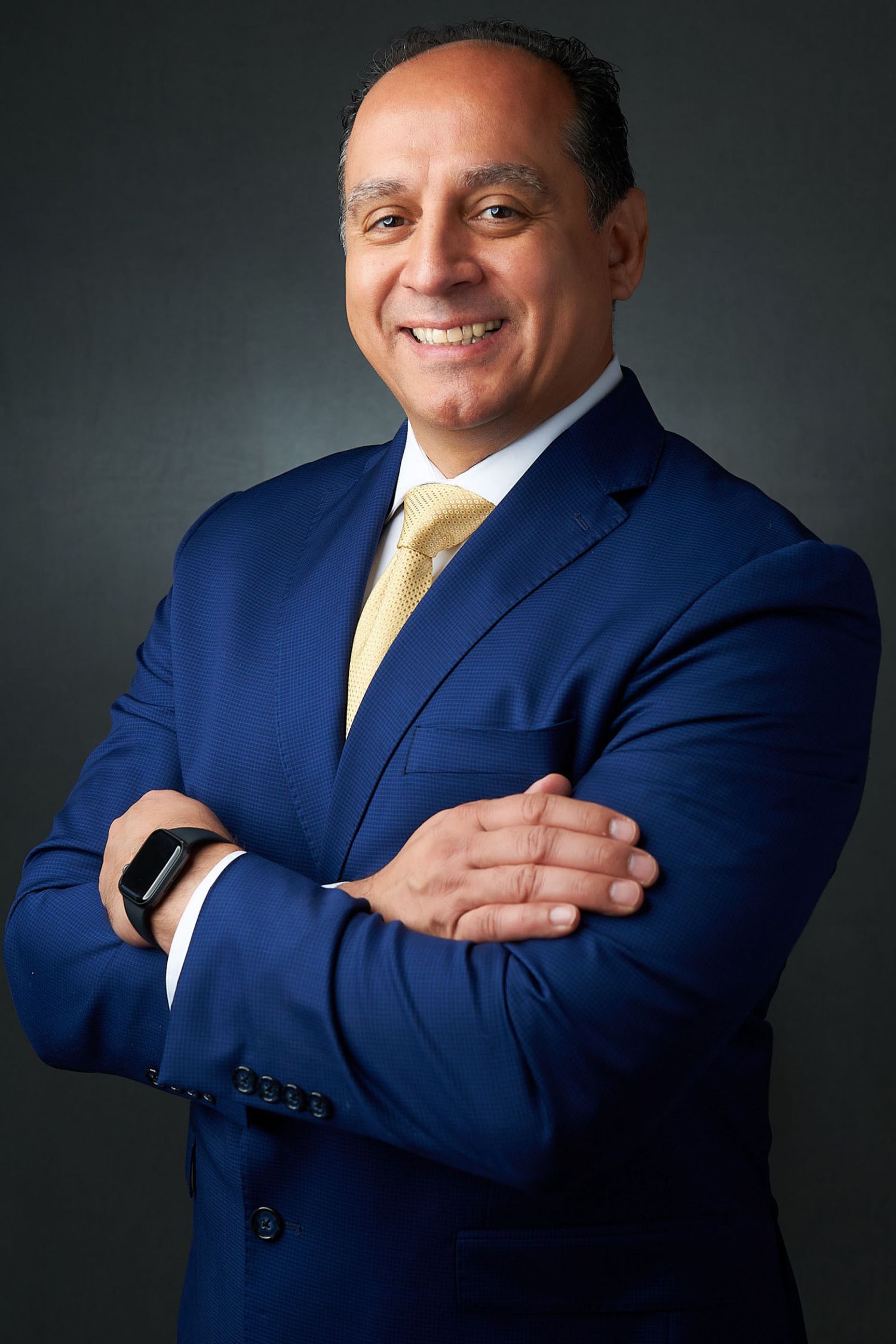 Confident businessman in blue suit and gold tie posing with arms crossed for professional portrait.