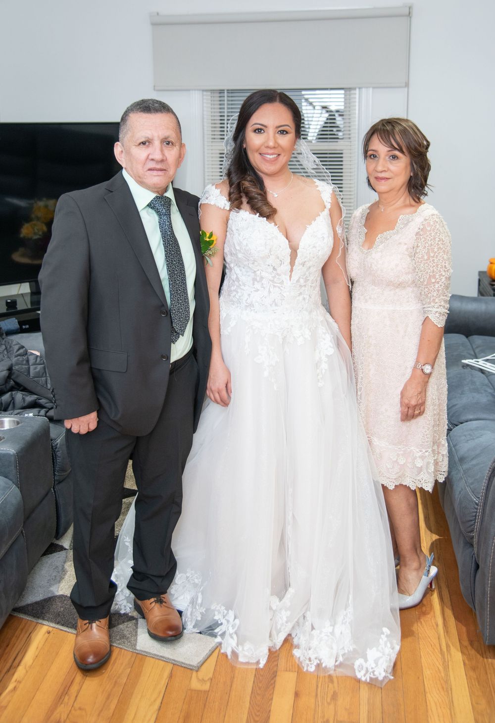 A formal wedding party poses together in white lace dresses and dark suits on a hardwood floor.