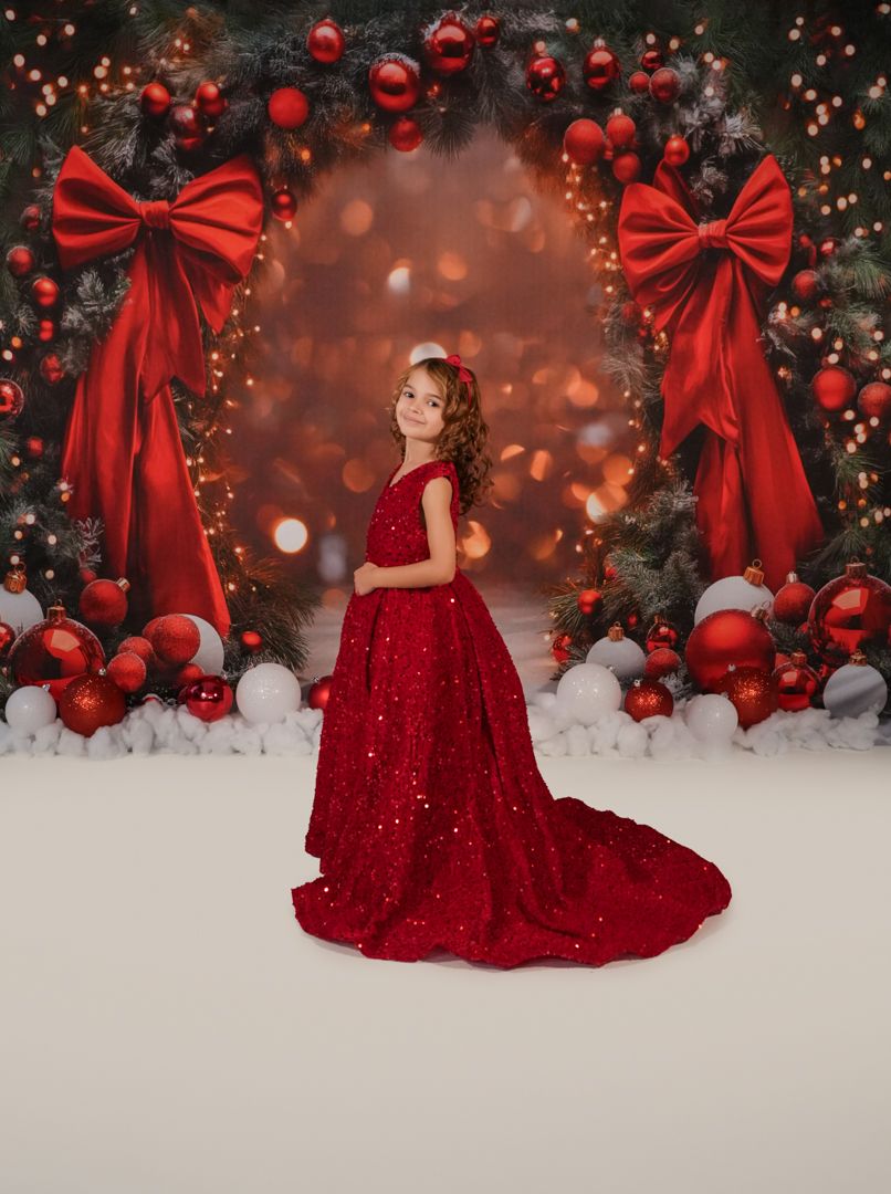 A stunning red sequined gown glimmers against a Christmas backdrop with ornaments and large red bows.