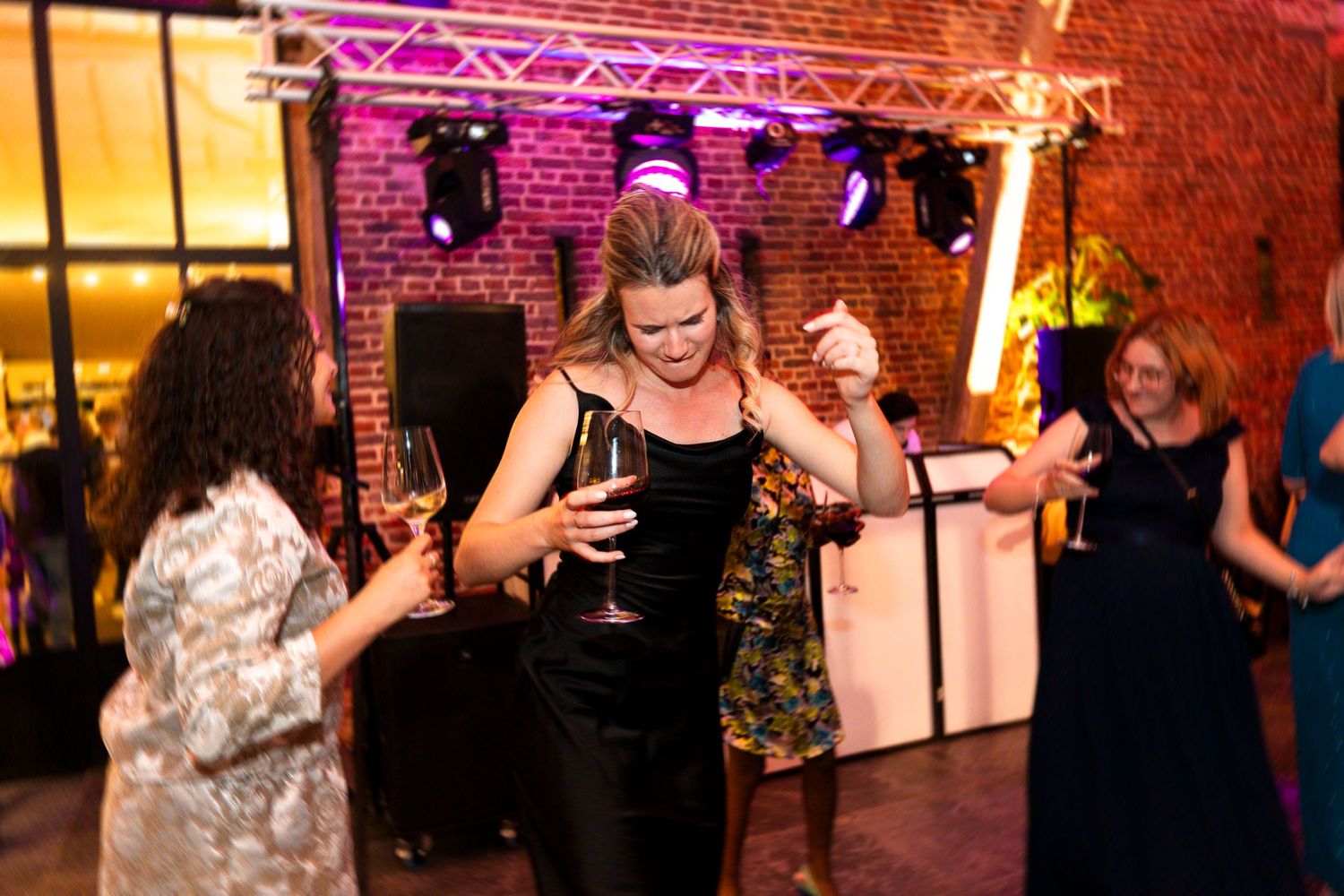 Party guests dancing and celebrating at a lively reception with colorful lighting and exposed brick walls.