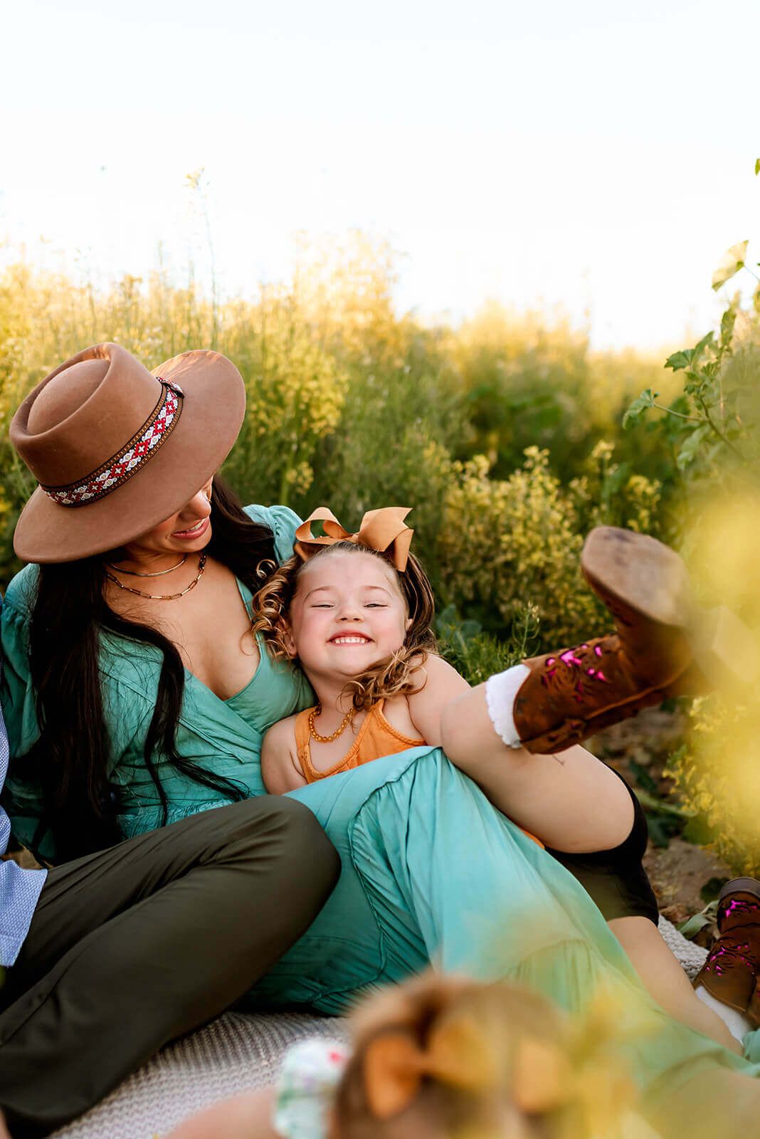 Romantic couple in turquoise and olive outfits share tender moments while relaxing on a blanket at sunset.