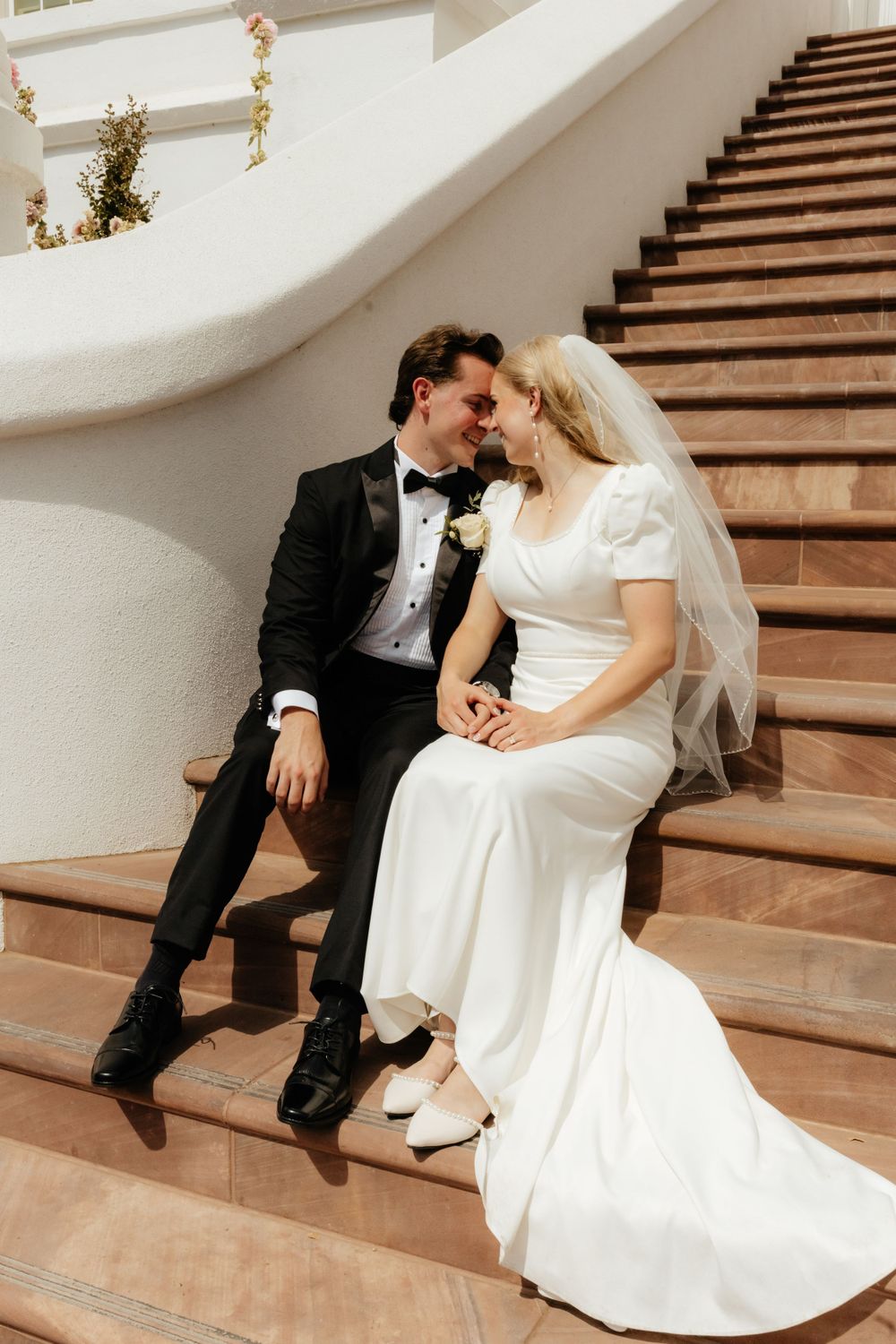 Bride and groom sit closely together on elegant curved staircase sharing an intimate moment.