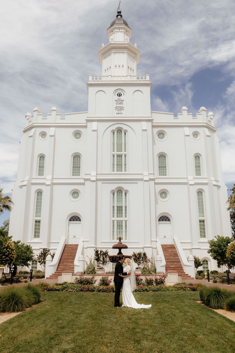 Wedding couple embracing in front of a grand white LDS temple on their wedding day.