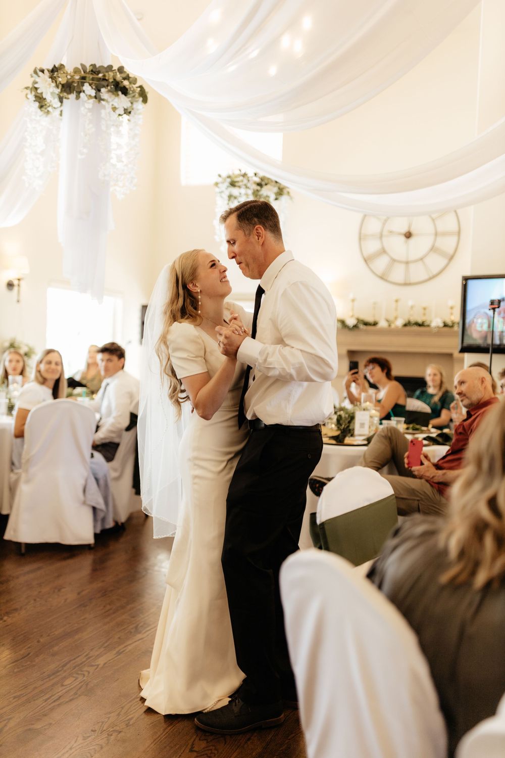 Bride and groom share first dance under white draping in a warmly lit wedding reception venue.