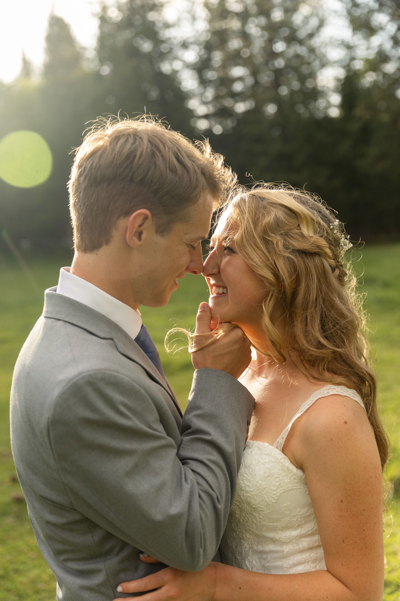 a couple nose-to-nose with the sun glistening behind them in natural colors. engagement photography