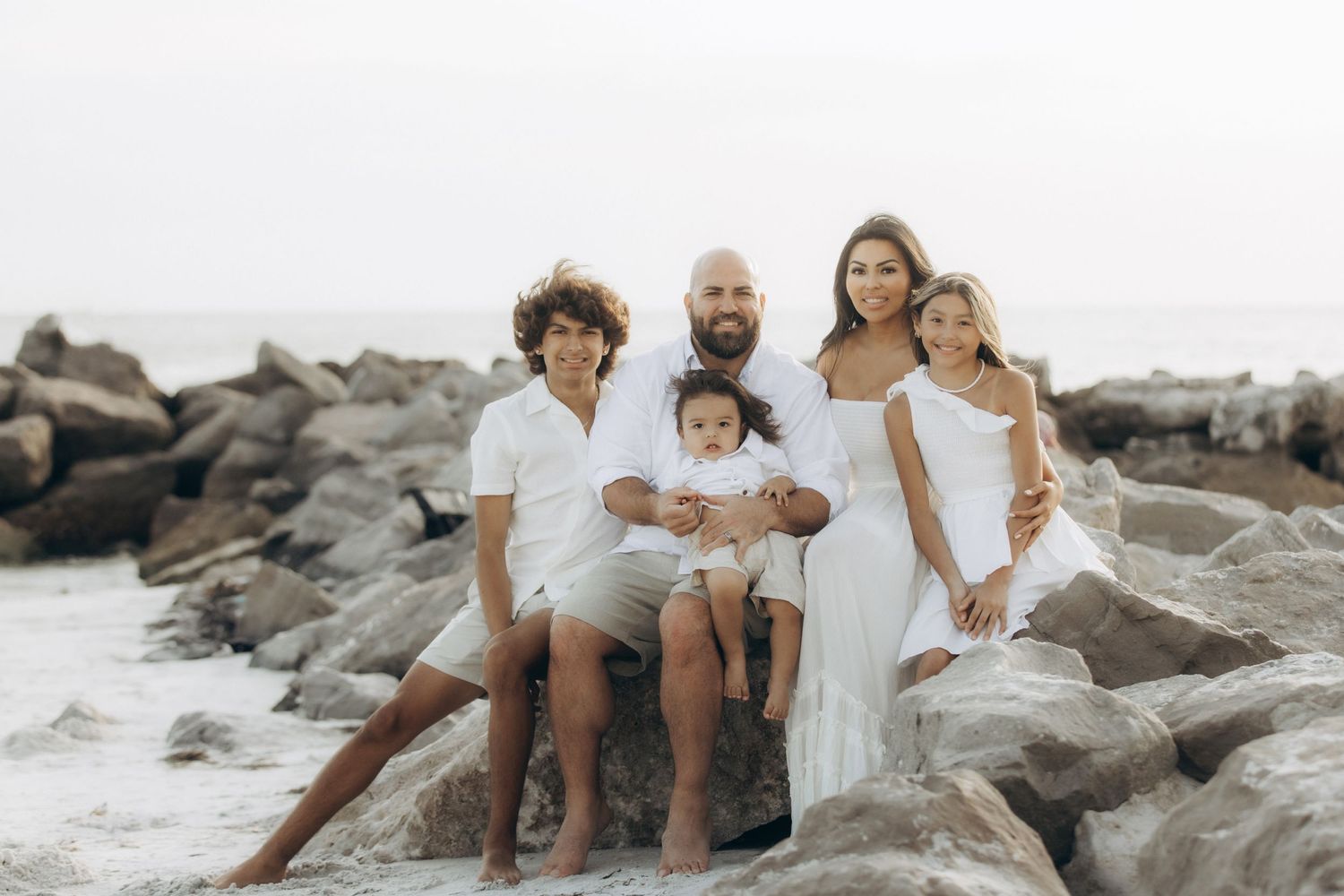 A family sitting together on rocky coastal terrain during a lifestyle photoshoot.