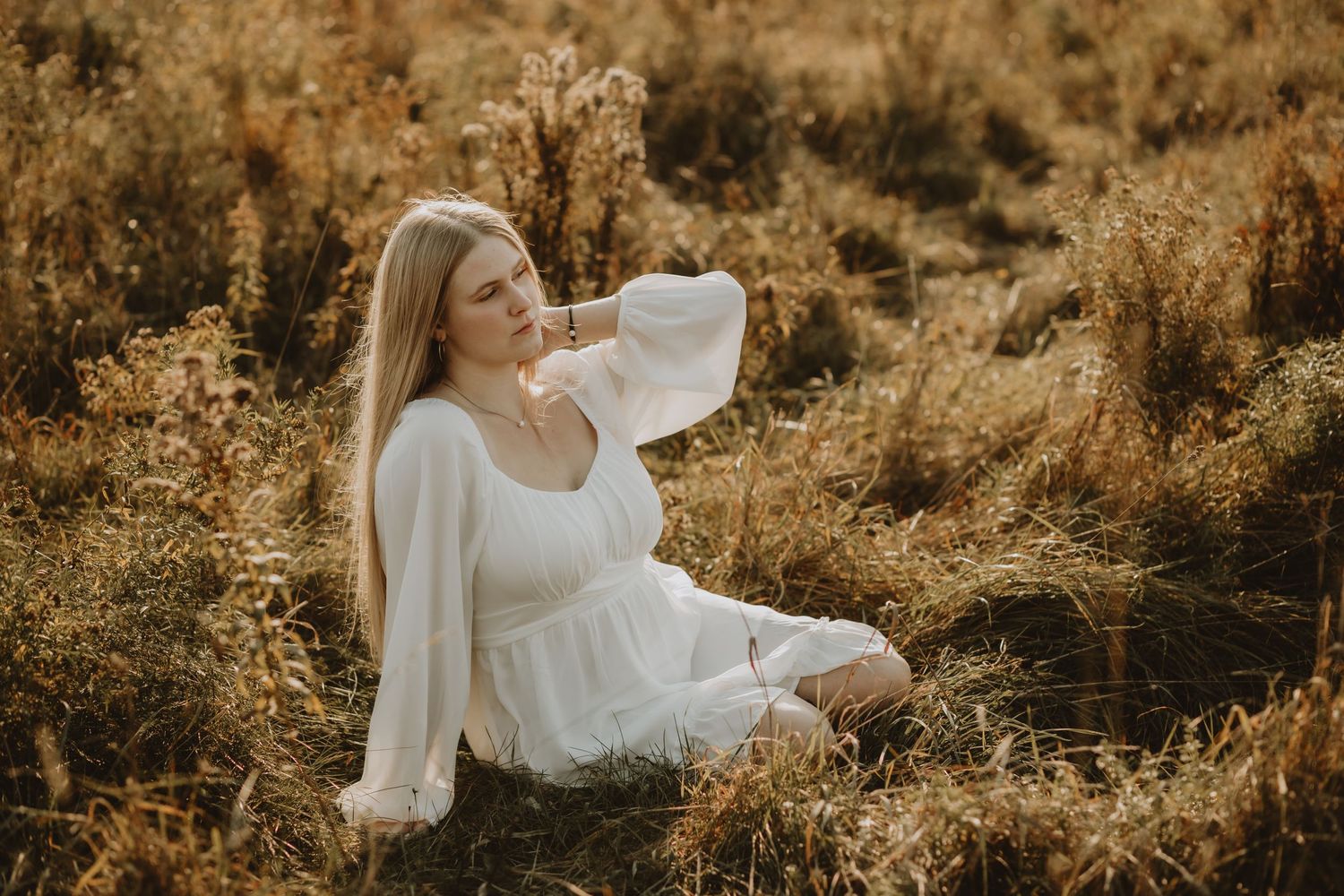 A woman in a flowing white dress poses elegantly in a golden field at sunset.