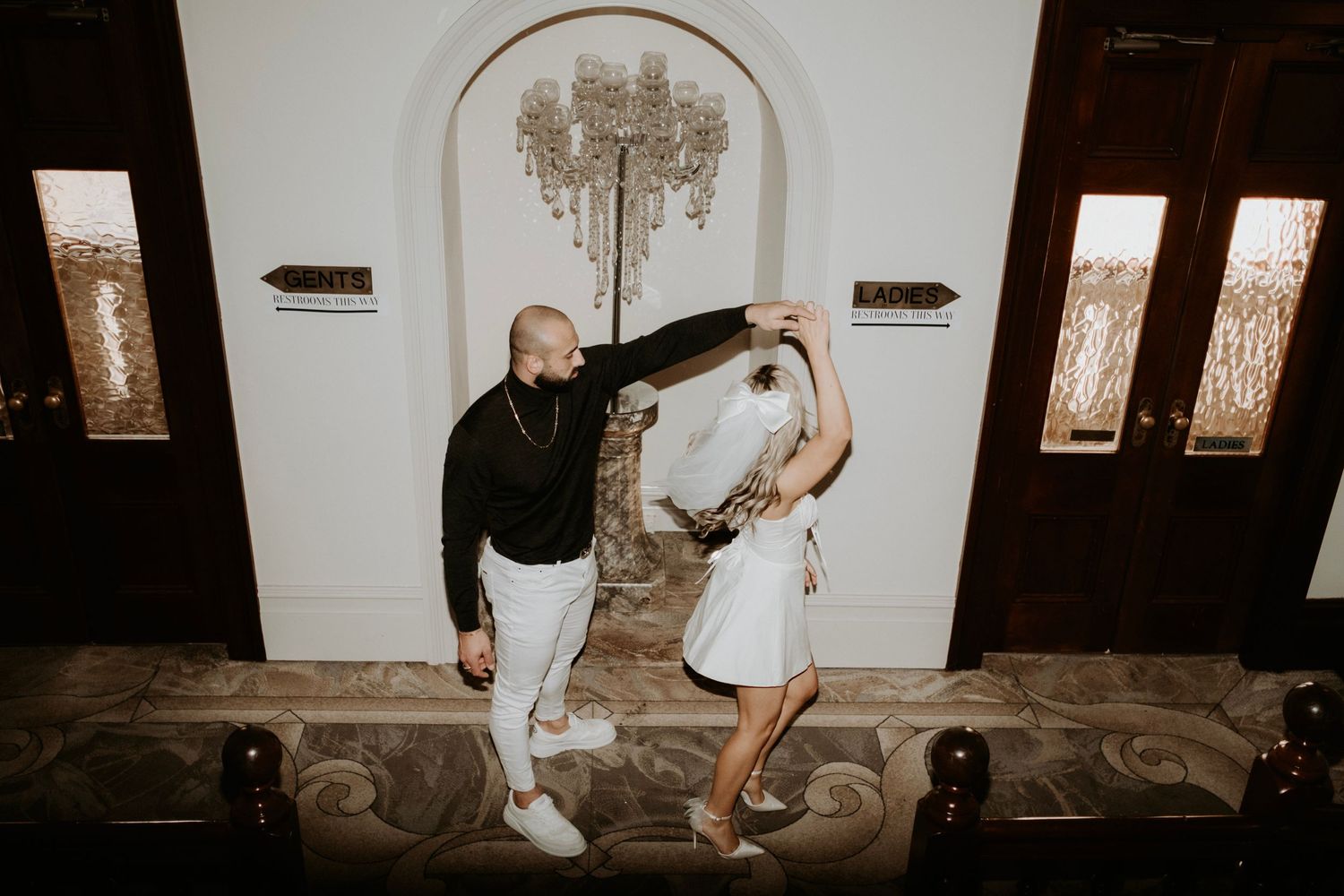 Playful couple in black and white outfits dance together under arched doorway.