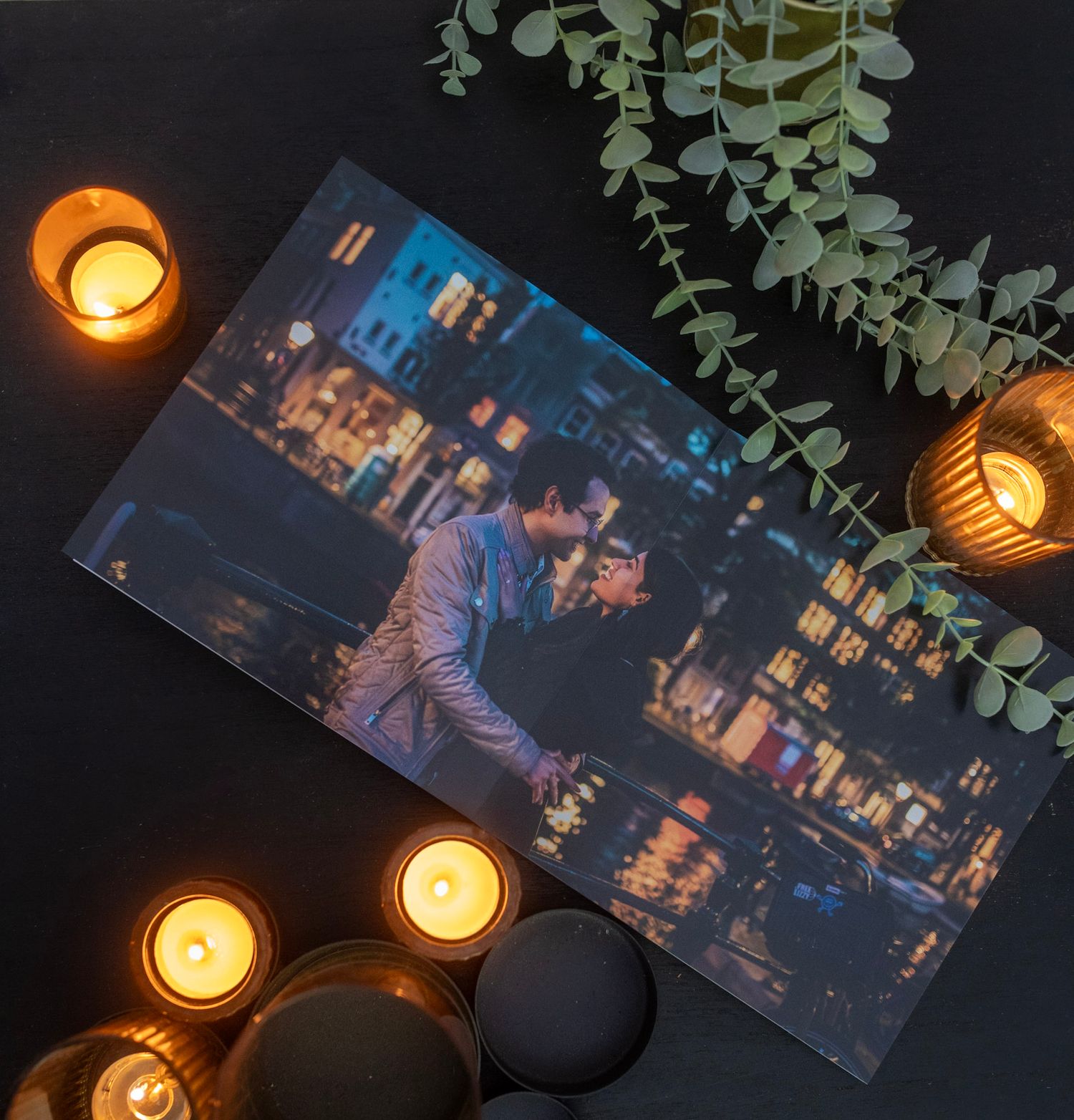 Lit candles illuminate a dark room with eucalyptus leaves, a picture album laid on the table